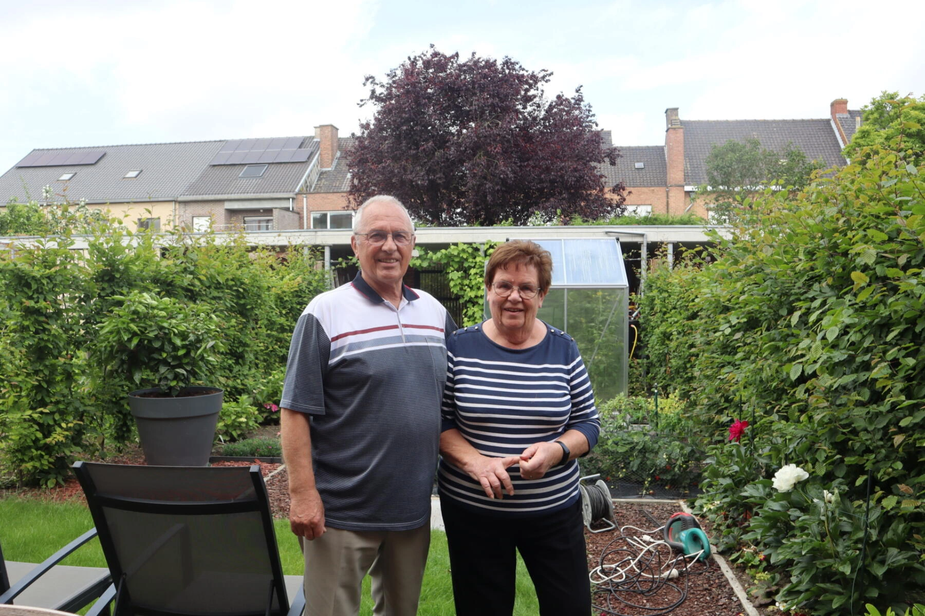 De bewoners Roland en Christine poserend in hun groene tuin.