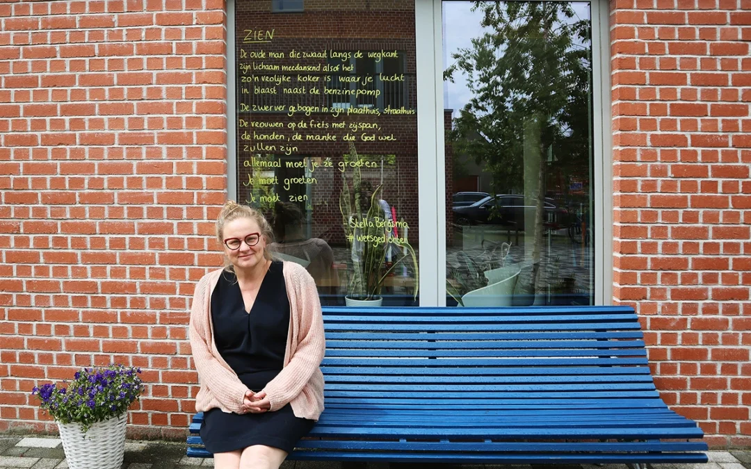 Bewoner Sara zit op een bank voor haar huis met een gedicht op het raam